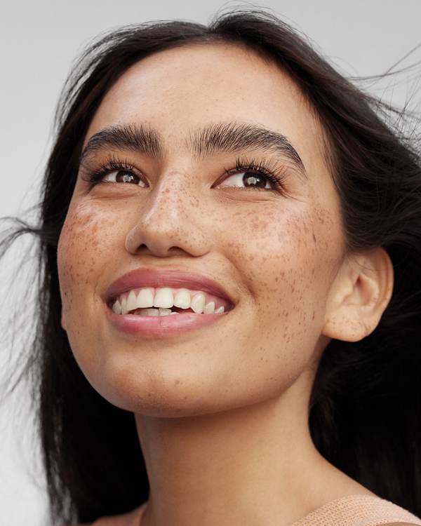Laughing model with freckles and wind-swept dark hair — Paul Mitchell Clean Beauty