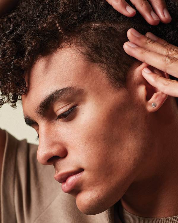 Model with short dark curls, fingers at his temple — MITCH by Paul Mitchell