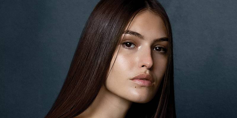 Model with long, sleek dark brown hair against a deep blue backdrop — Paul Mitchell Neuro