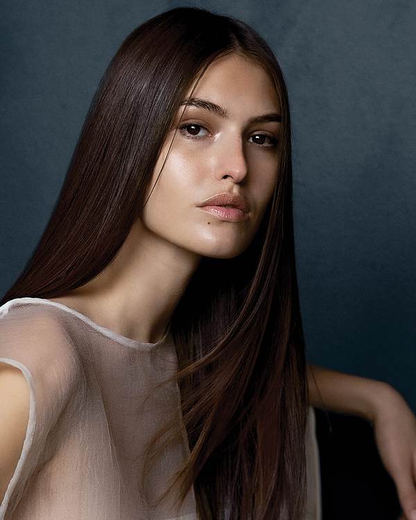 Model with long, sleek dark brown hair against a deep blue backdrop — Paul Mitchell Neuro
